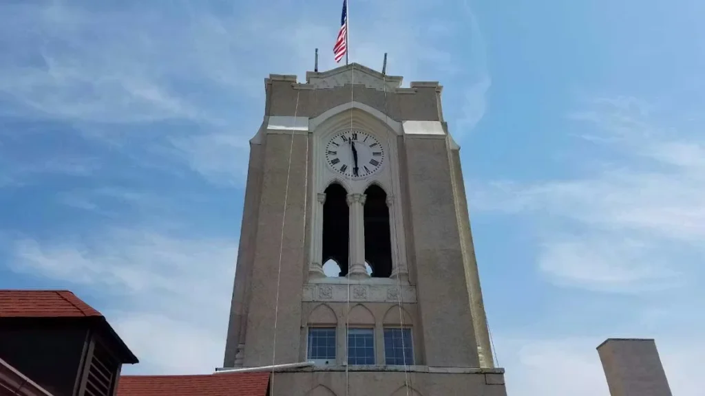Historic clock tower with American flag flying above, featuring arched openings and clock face against a blue sky.
