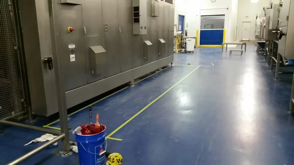 Industrial food processing area with blue epoxy floor coating, stainless steel equipment, and marked safety lines during floor maintenance.