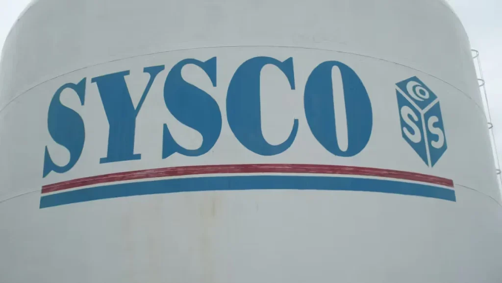 Large industrial storage tank painted white with SYSCO company logo and branding displayed on the exterior.