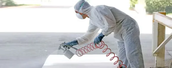 Commercial painter wearing protective coveralls and respirator while spray painting a surface using a spray gun, demonstrating overspray control.