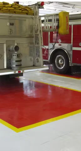 Fire station bay with a fire truck parked on a red-and-white epoxy floor featuring yellow safety striping.