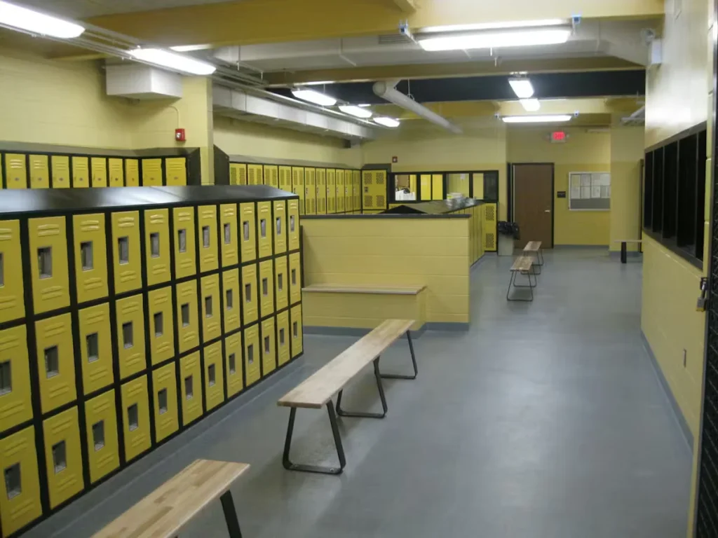 Freshly painted school locker room with yellow lockers, gray epoxy floor, wooden benches, and bright overhead lighting.