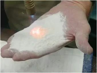 Hand holding white reflective roof coating granules, demonstrating heat-reflective, energy-efficient roofing material.