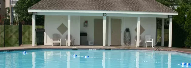 Outdoor swimming pool with clear blue water in front of a small pool house, illustrating a resurfaced and well-maintained pool area.