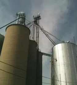 Agricultural grain silos and feed handling equipment at a farm facility, highlighting industrial painting and maintenance of farm and ranch buildings.