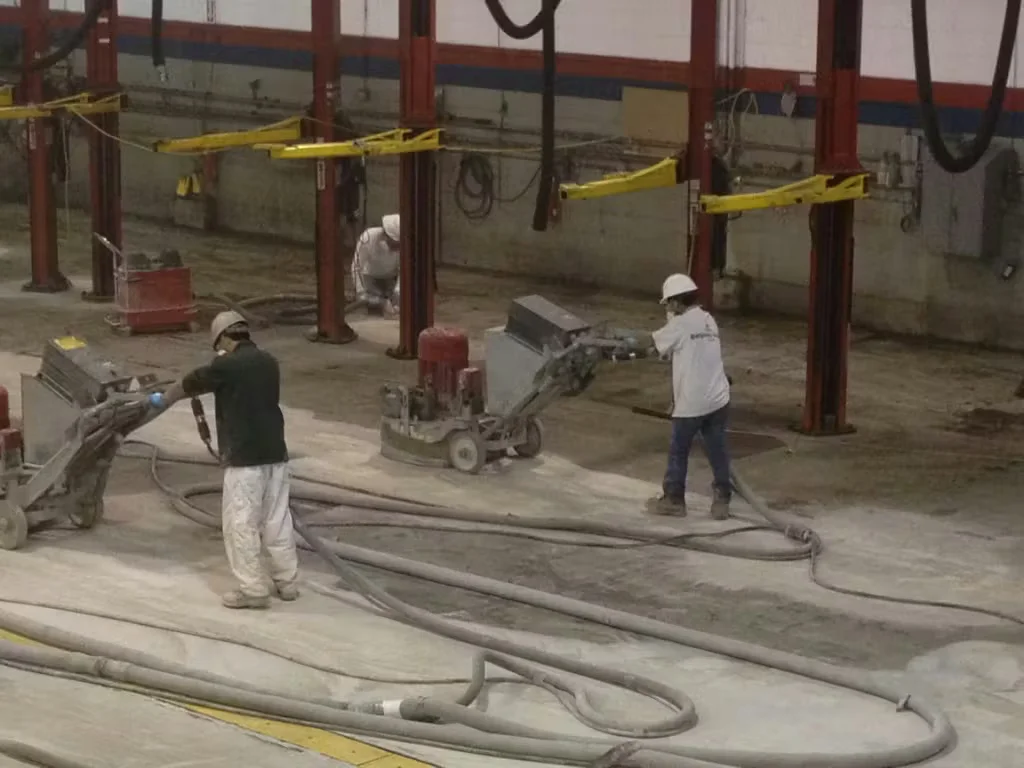 Industrial workers using diamond grinding machines to remove old concrete floor coatings inside a large commercial facility during surface preparation.