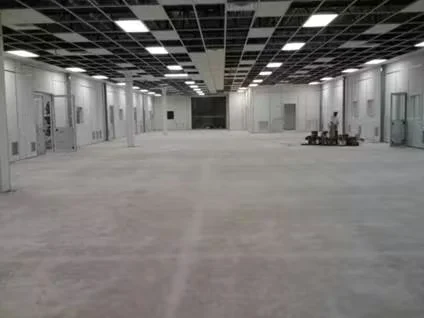 Large empty commercial interior with unfinished concrete flooring, white walls, multiple doors along the sides, and a grid-style ceiling with recessed lighting, prepared for an epoxy floor coating project.
