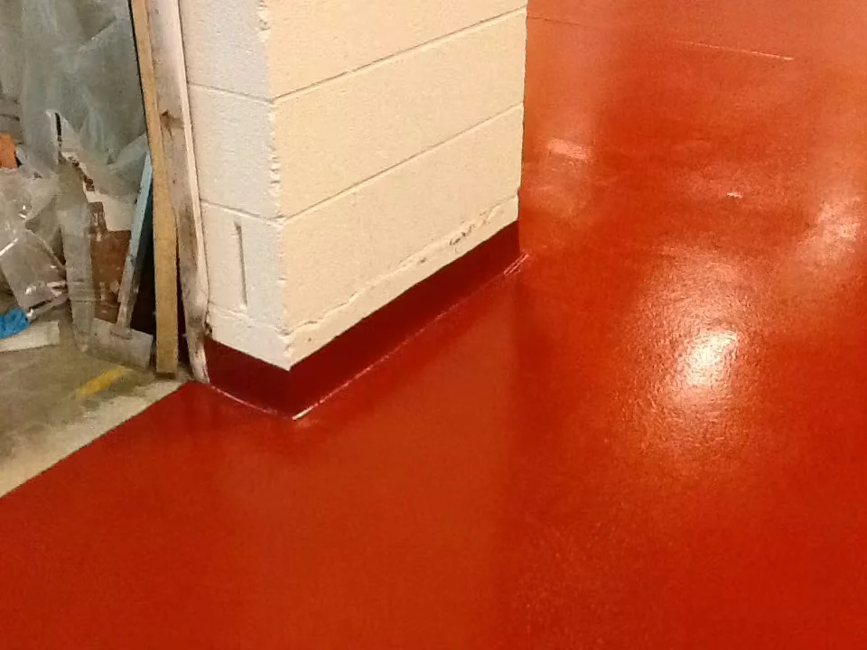 Red epoxy floor with a matching cove base seamlessly applied at the base of a white concrete block wall.