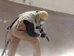 Worker in protective gear using a jackhammer to prepare a concrete surface by removing damaged material.