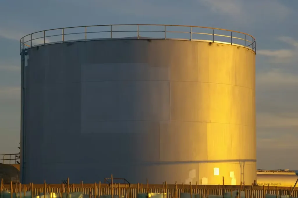 Large cylindrical industrial storage tank with protective coating, illuminated by golden sunlight at an industrial facility.