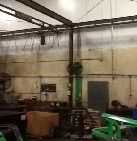 Industrial facility interior with heavy machinery, overhead steel beams, hanging cables, and stained walls prior to professional industrial cleaning.
