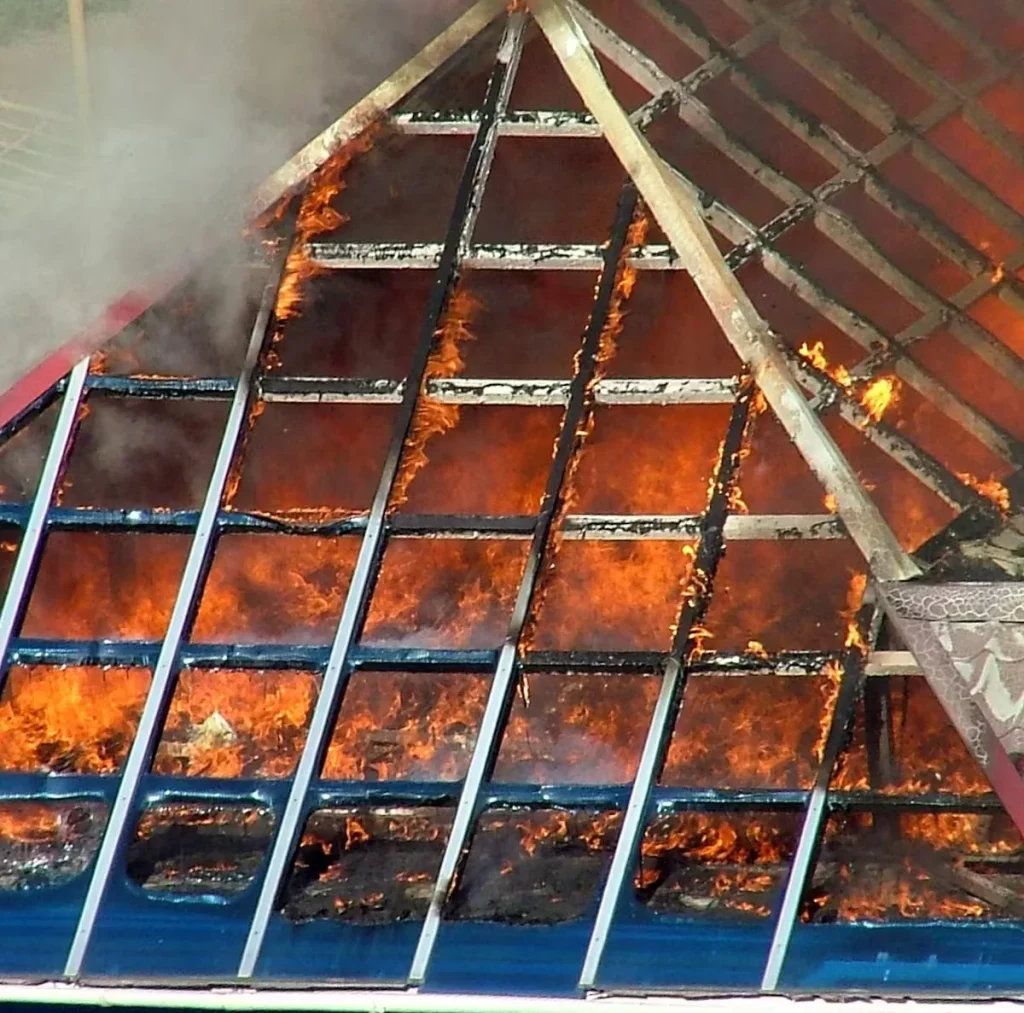 Intumescent fireproof coating expanding and charring on a building roof structure during a fire, protecting the underlying materials.