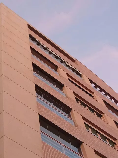 Multi-story commercial building exterior with brick and stucco facade, balconies, and windows, viewed from a low angle during daylight.