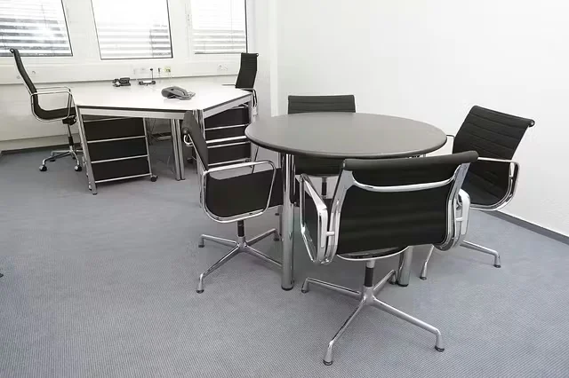 Modern office interior with neutral gray flooring, round meeting table, black office chairs, and a minimalist workstation by a window.