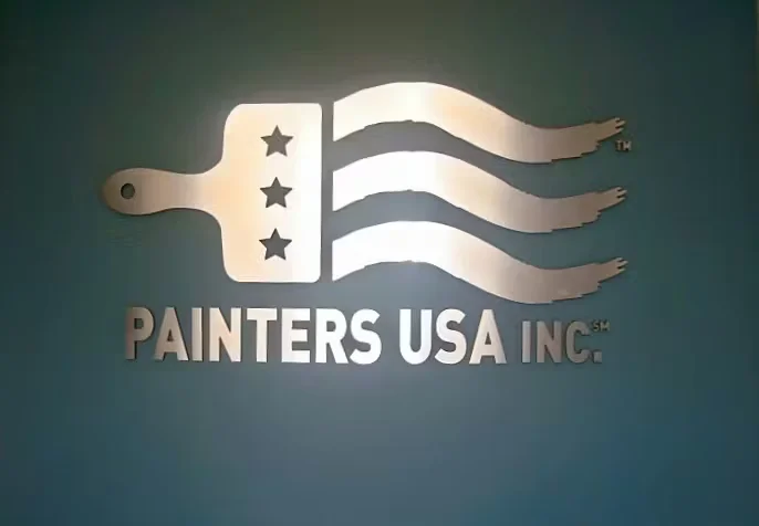 Painters USA Inc. logo mounted on a teal wall, featuring a paintbrush with stars and flowing stripes in a metallic finish.