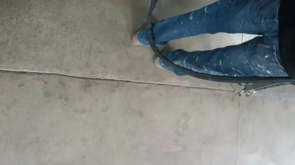 Technician filling a concrete floor expansion joint with a polyurea system, with application hose visible over industrial concrete flooring.