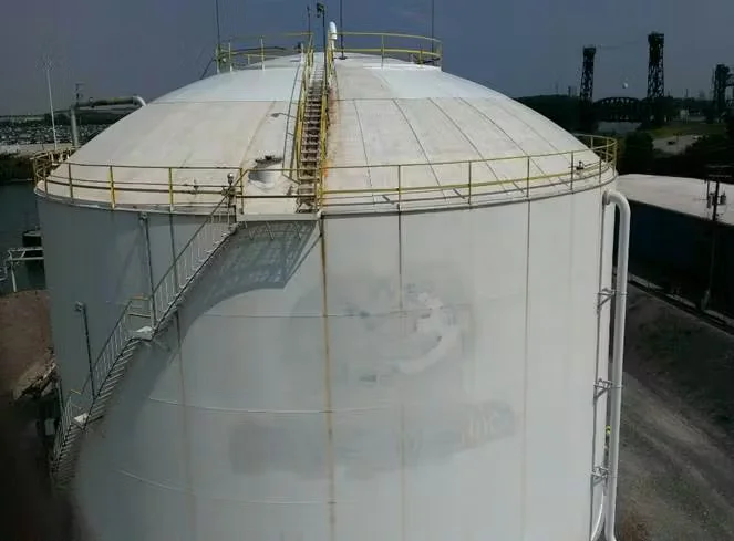 Large white storage tank at a chemical plant, featuring exterior staircases, safety railings, and an industrial facility in the background.