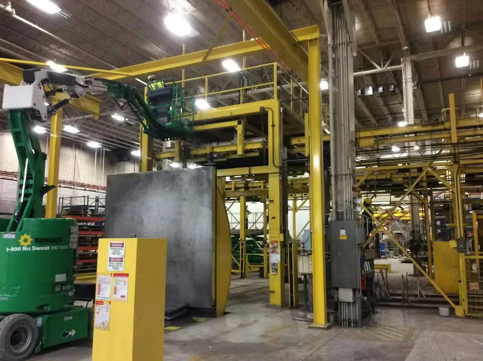 Interior of a large industrial distribution center with yellow steel structures, overhead machinery, and a green lift being used for maintenance or painting work.