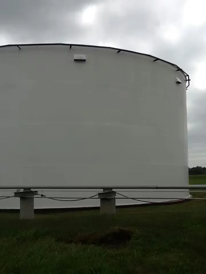Large white industrial storage tank at an ethanol plant, freshly cleaned, with overcast sky and grassy surroundings.
