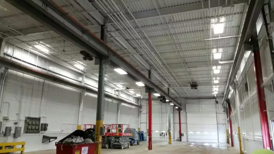 Interior of a large industrial warehouse with high ceilings, exposed steel beams, overhead lighting, and open floor space prepared for industrial painting or flooring work.