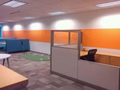 Modern office interior with orange accent wall, cubicles, desks, and overhead lighting, showing a freshly painted commercial workspace.
