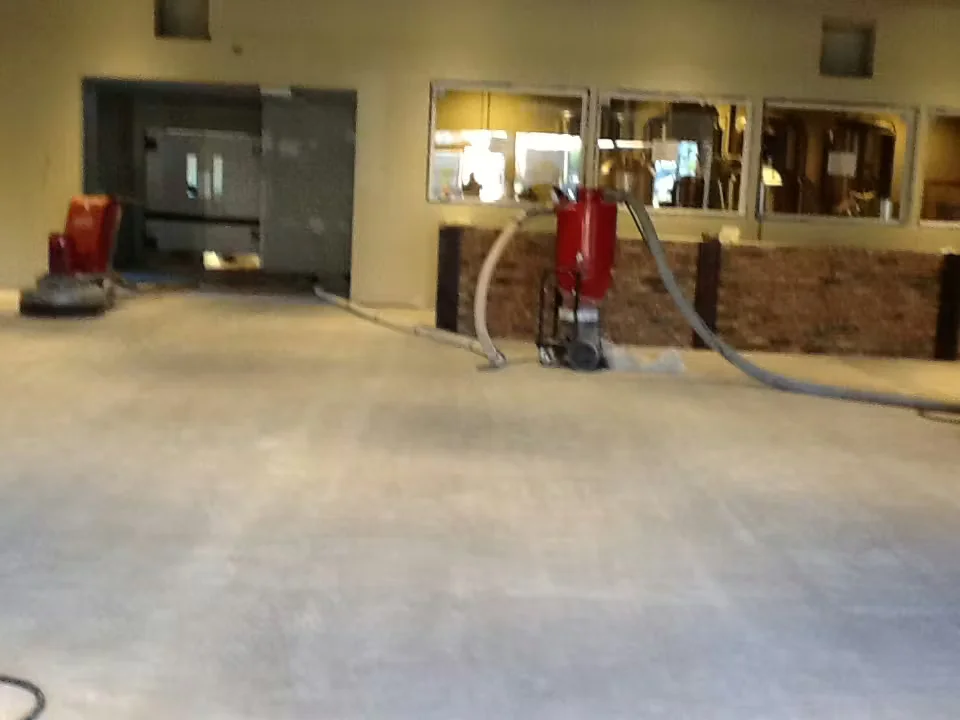 Industrial facility floor preparation in progress with concrete grinding and dust collection equipment before coating or polishing.