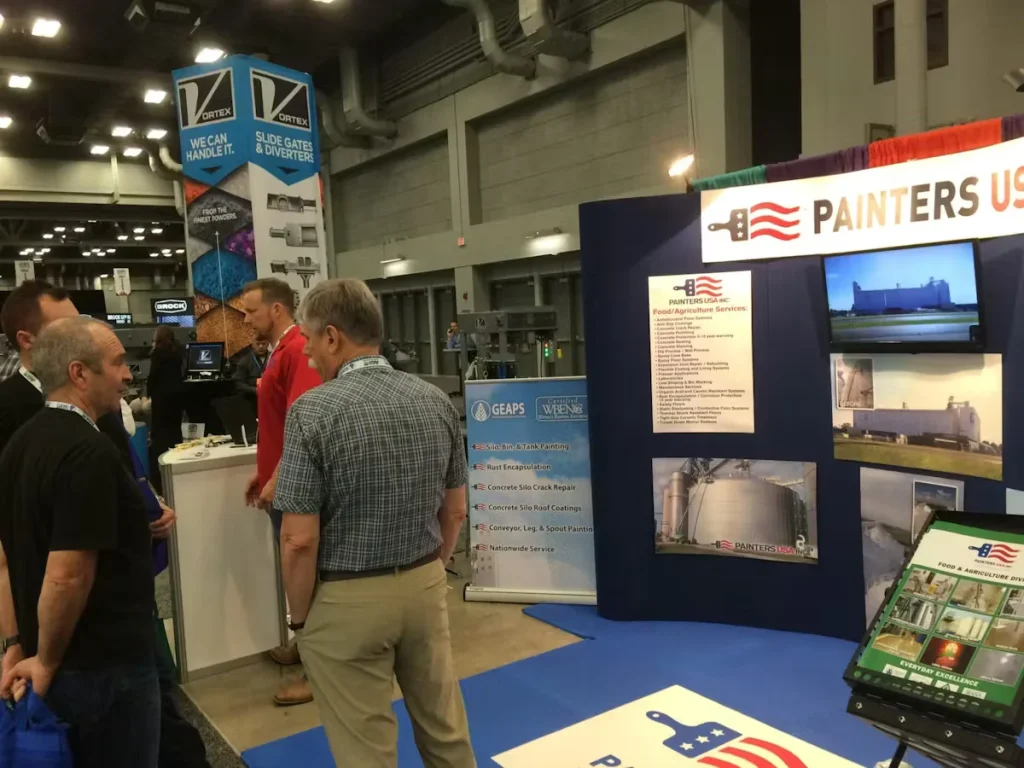 Painters USA Inc. trade show booth at the GEAPS Exchange, showcasing industrial and agricultural painting services and silo coating projects while attendees network.