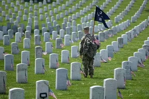 U.S. service member walking through a military cemetery with rows of headstones and American flags, honoring fallen soldiers.
