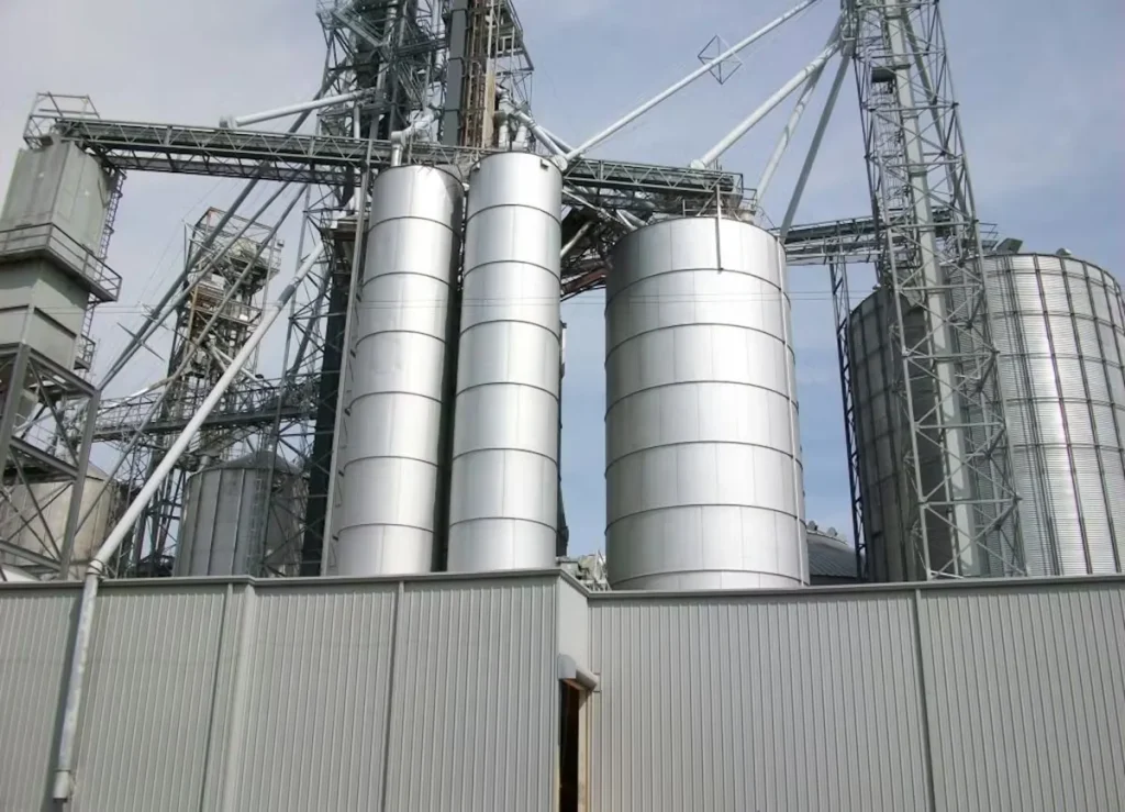 Industrial grain silos and steel conveyor structures at an agricultural processing facility after industrial painting and concrete services.