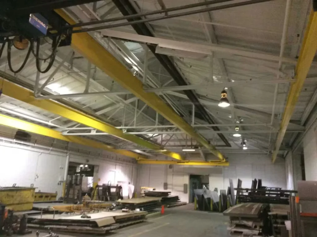 Clean industrial facility interior with freshly painted ceiling, yellow overhead crane beams, and organized equipment, highlighting the difference between industrial cleaning and painting services.