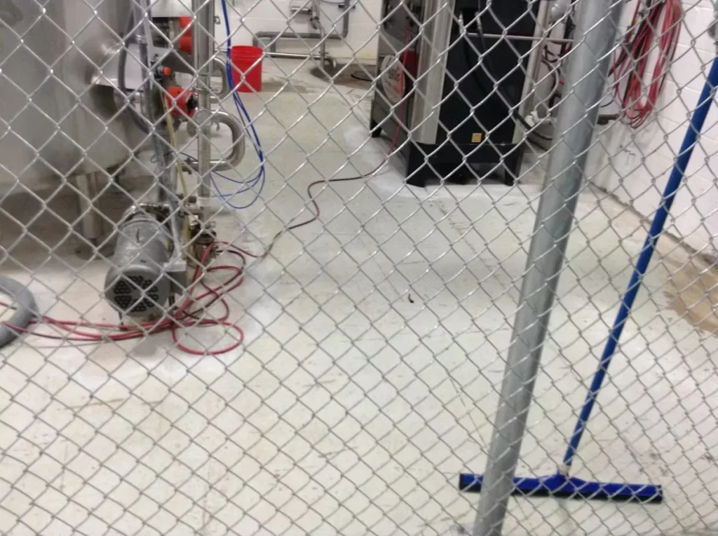 Urethane cement floor installation in a food processing plant, showing industrial equipment behind a chain-link barrier and freshly coated flooring in Illinois.