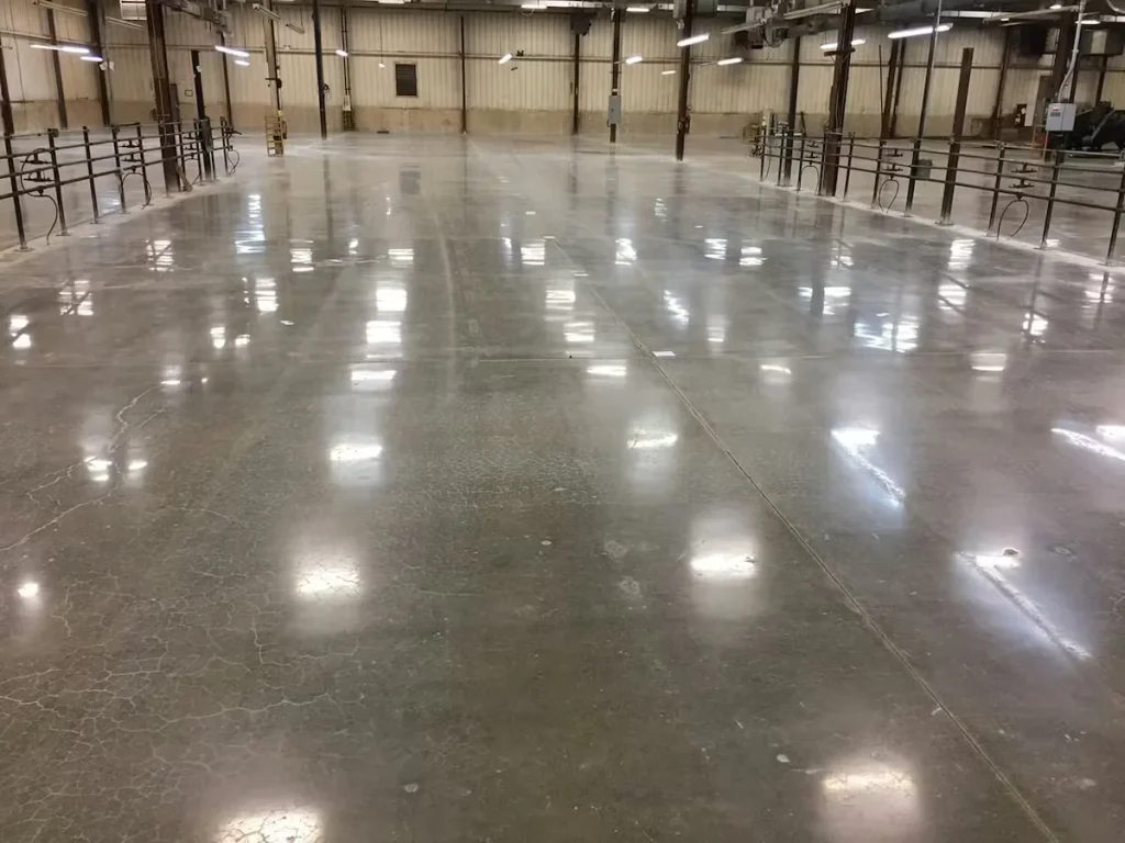 Large industrial warehouse with a polished concrete floor, reflecting overhead lights and showcasing a smooth, high-gloss finish across the open space.