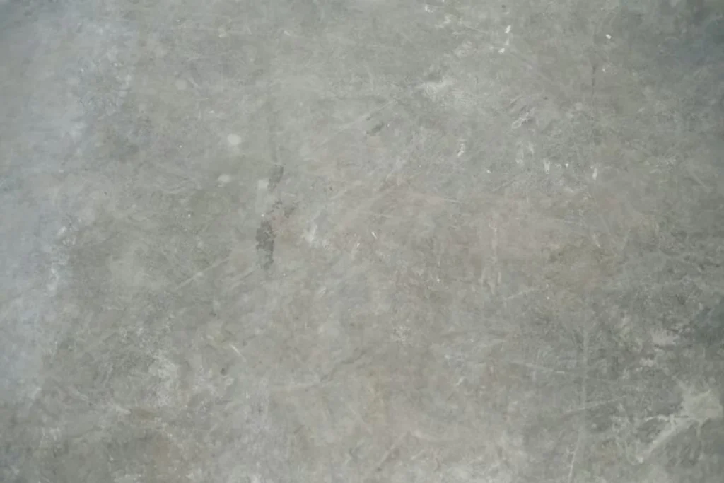 Close-up of a worn gray concrete floor with scuffs, scratches, and faint stains across the surface.