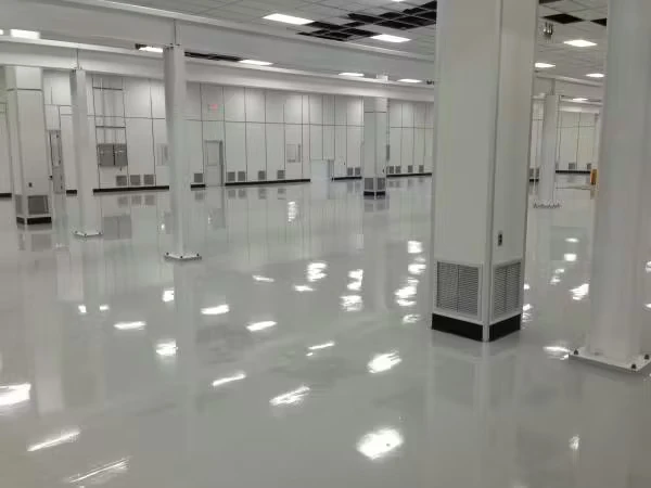 Large empty industrial interior with white columns and wall panels, bright overhead fluorescent lights, and a smooth glossy light-gray floor reflecting the ceiling lights.