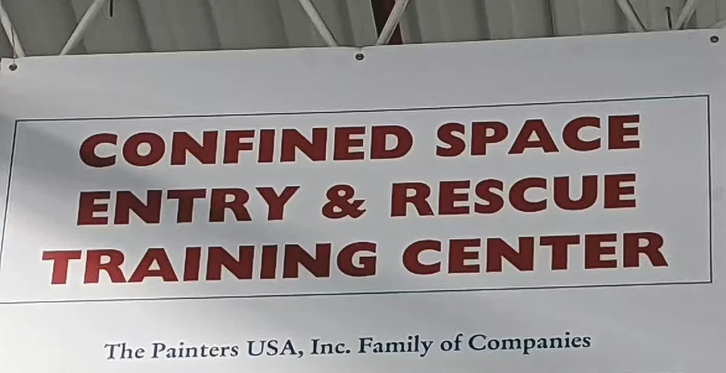 Large indoor banner reading “Confined space entry and rescue training center,” with smaller text below that says “The Painters USA, Inc. Family of Companies.”