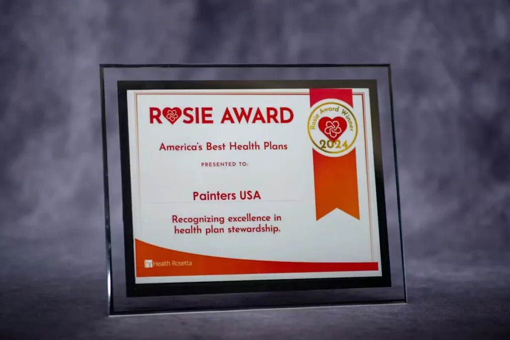 Framed “Rosie Award” plaque from America’s Best Health Plans presented to Painters USA, with a “Rosie Award Winner 2024” badge and the text “Recognizing excellence in health plan stewardship,” on a gray backdrop.