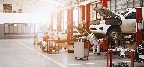 Automotive repair shop with multiple cars lifted on red hydraulic lifts, mechanics working, and tools spread across the bright, open workspace.