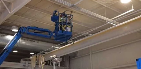 Combustible dust cleaning—technician on a lift vacuuming and removing dust buildup from high overhead beams.