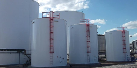 Group of large white ethanol storage tanks outdoors, each with red safety ladders and platforms, under a bright blue sky.