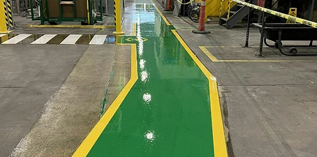 Freshly painted bright green walkway with yellow safety borders inside an industrial facility, marked for clear pedestrian pathways.