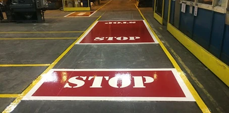 Floor marking and line painting—brightly painted red stop signs and yellow lines on a warehouse floor for safety guidance.