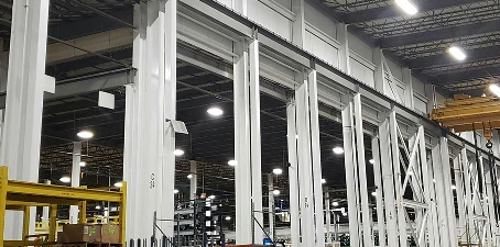 Factory interior with tall steel support beams and walls freshly painted white, illuminated by bright overhead lights.