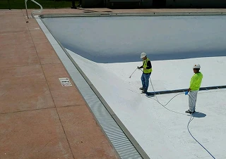 Municipal industry workers in safety gear spraying coating inside an empty swimming pool.