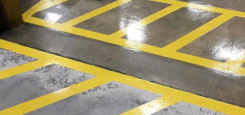 Freshly painted bright yellow safety lines marking designated pathways on a polished concrete floor.