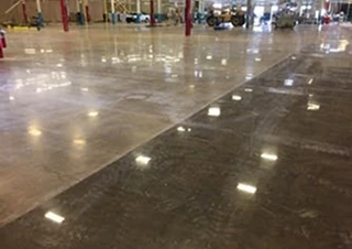 Shiny polished concrete floor inside a large industrial space with reflective overhead lighting.