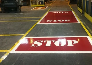 Factory floor with freshly painted yellow safety lines and red stop zones marked in bold white letters.