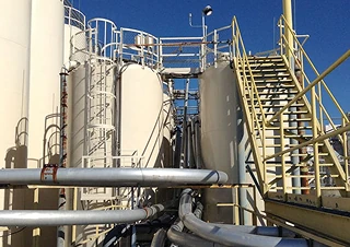 Large outdoor industrial tanks with ladders, stairways, and connecting pipes, prepared for protective coating or painting.