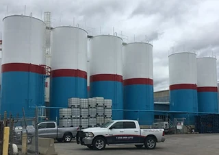 Multiple tall storage silos painted white with blue and red bands, located in an outdoor industrial yard.