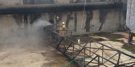 Wet and vapor blasting—worker in protective gear using pressurized water and vapor to clean a large industrial surface.