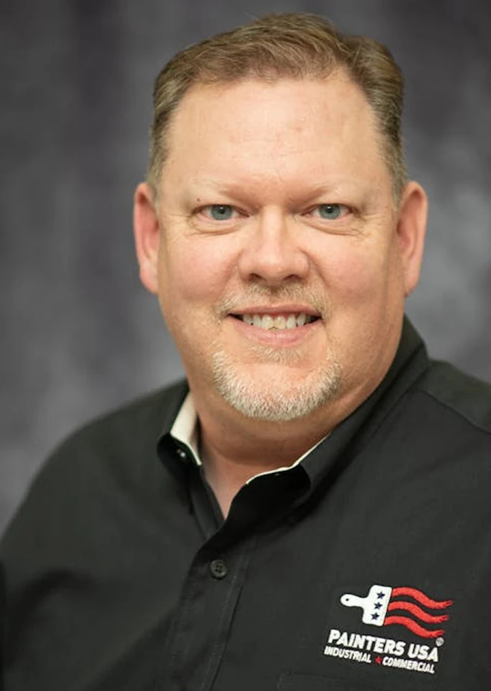 Photo Portrait of Darren Lottes wearing a black shirt with a Painters USA logo embroidered over his heart.